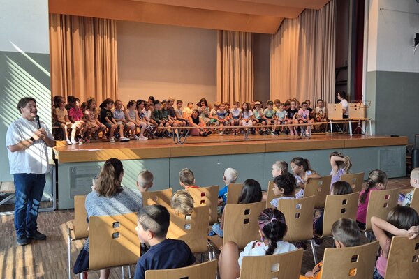 Nach der Begrüssung des Schulleiters, Simon Wullschleger sitzen alle Schulkinder der 1. Klasse und 2. Klasse auf der Bühne.